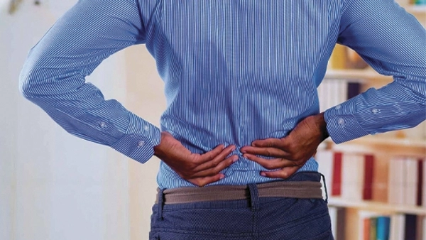 Individual in a blue shirt holding their lower back, indicating pain.